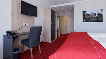 A hotel room with a desk, chair, TV, bed, and a red carpet.