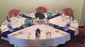 A round dining table set for six with white tablecloths, blue napkins, and matching glassware.