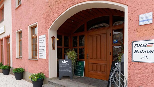 A pink building with a wooden door and a sign for 'DKB Bahnen'. - Hotel Stadt Magdeburg (Perleberg)