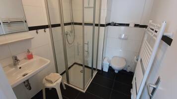 A bathroom with a glass-enclosed shower, a sink with a soap dispenser, a toilet, and a radiator.