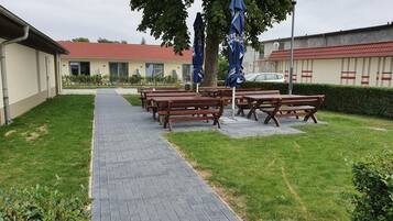 Un camino pavimentado que lleva a mesas de picnic y sombrillas, con un edificio al fondo.