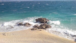 A beach with clear turquoise water, pebbly sand, and rocky outcrops.