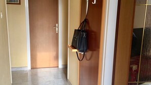 A hallway with a wooden door, a coat rack with a bag, and a tiled floor.