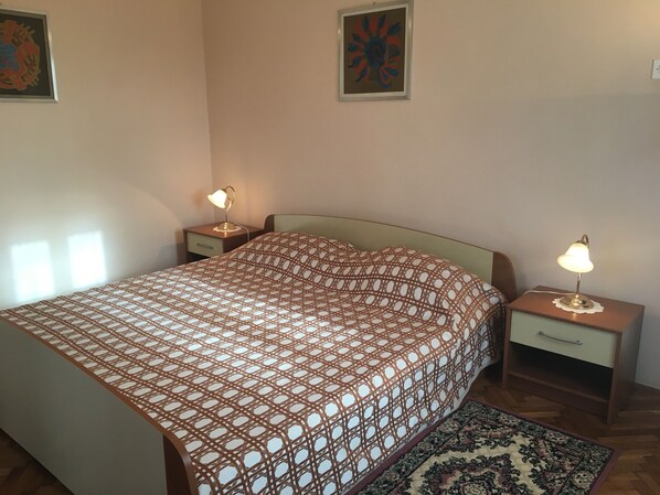A bedroom with a patterned bedspread, two bedside tables with lamps, a nightstand, and a patterned rug.