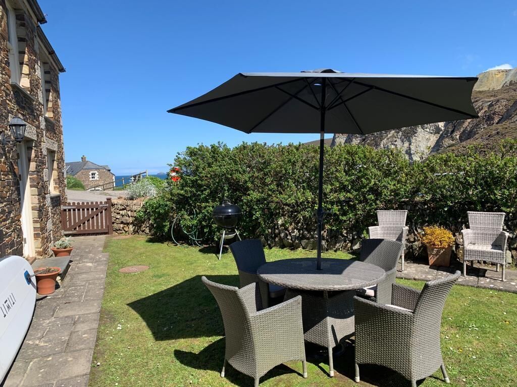 A patio with outdoor furniture, a large umbrella, and a view of the sea.
