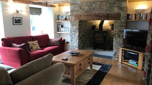 Ein gemütliches Wohnzimmer mit Kamin aus Stein, einem roten Sofa, einem Holztisch und einem Fernseher auf einem Holzschrank.