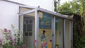A glass-enclosed structure with a mural of a person on a bicycle, surrounded by flowering plants. - house on garden, decorated by a painter, Pont Aven with 9kmwallo (Moëlan-Sur-Mer)