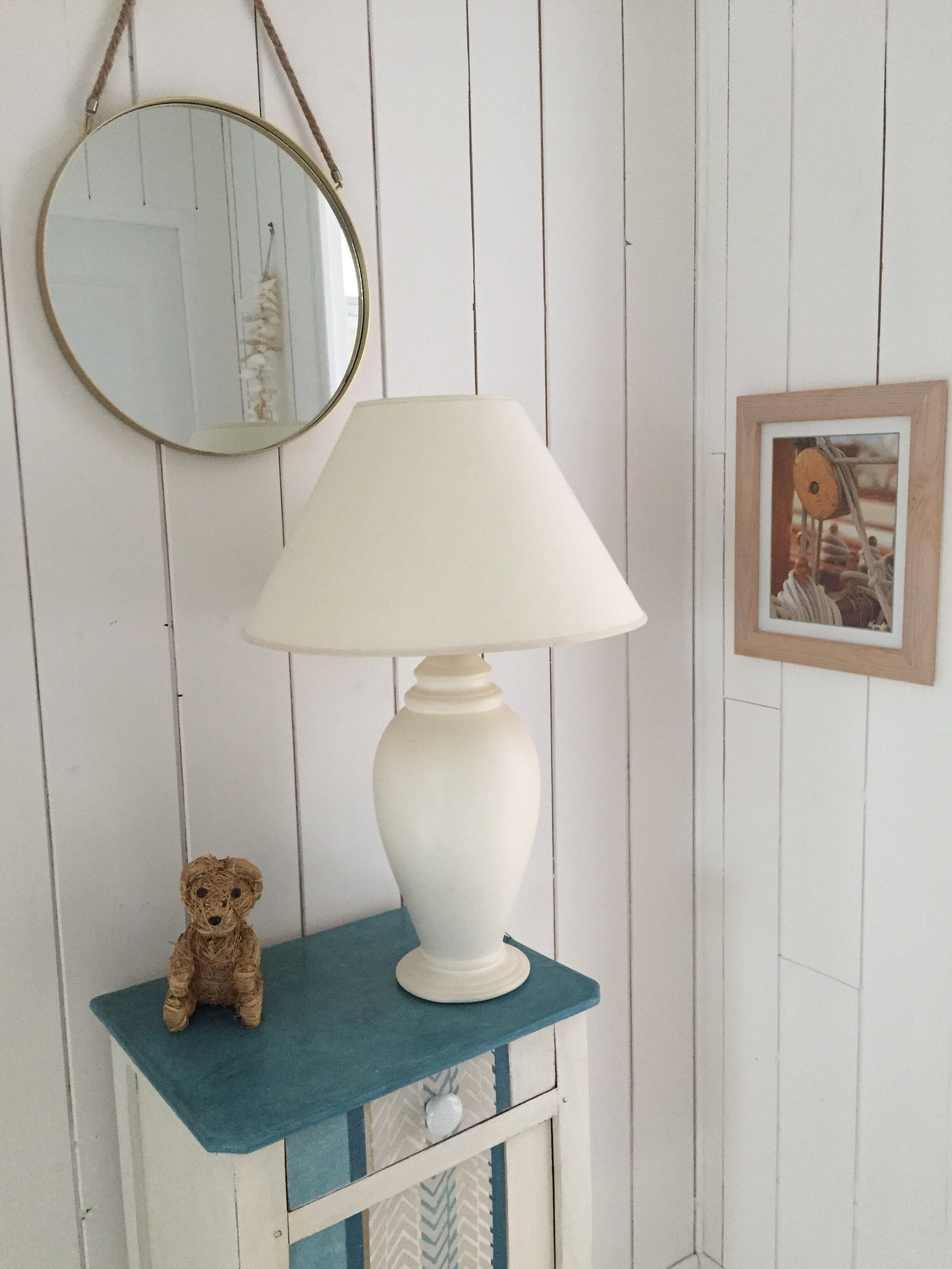 A white lamp with a white shade on a teal table against a white wooden wall.