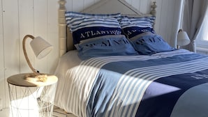 A bedroom with a bed, a bedside table, a lamp, and a woven rug. - house on garden, decorated by a painter, Pont Aven with 9kmwallo (Moëlan-Sur-Mer)