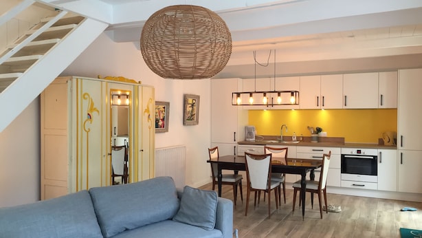 A modern living room with a sofa, dining table, chairs, and a kitchen area with white cabinets and a yellow backsplash. - house on garden, decorated by a painter, Pont Aven with 9kmwallo (Moëlan-Sur-Mer)