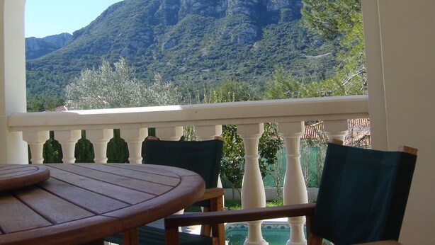 Een balkon met een houten tafel en stoelen, met uitzicht op een bergachtig landschap.
