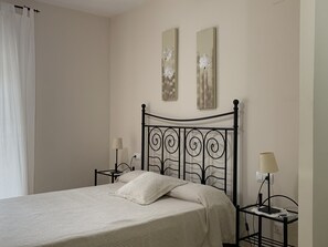 A neatly made bed with a patterned bedspread, two bedside tables with lamps, and two wall-mounted paintings.