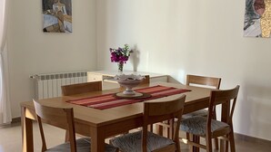 Een eethoek met een houten tafel en stoelen, een vaas met bloemen en twee schilderijen aan de muur.