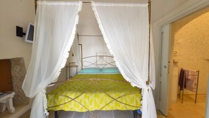 Ein Bett mit Baldachin, mit einer gelb gemusterten Tagesdecke und weißen Vorhängen.