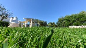 Ein grasbewachsenes Gelände mit einem weißen Gebäude, das ein kegelförmiges Dach und einen flach gedeckten Anbau hat.