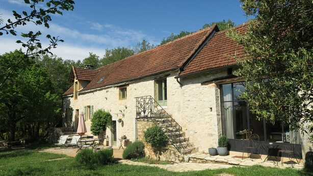 A stone house with a tiled roof, a staircase, and a patio with outdoor furniture.