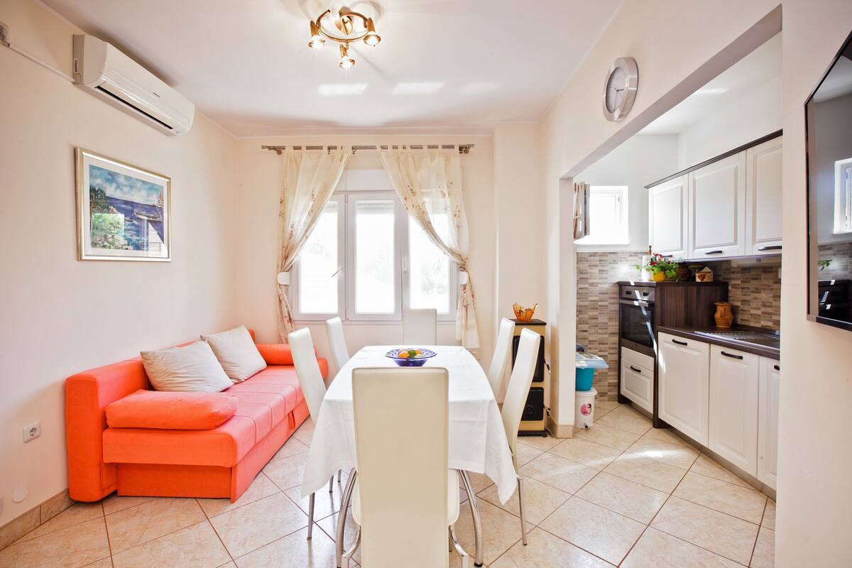 A modern kitchen with white cabinets, a built-in oven, and a countertop with a vase and fruits.