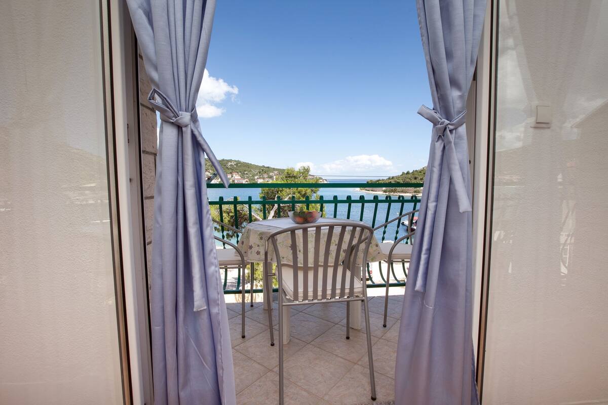A balcony with a table and chairs, overlooking a body of water and a bridge.