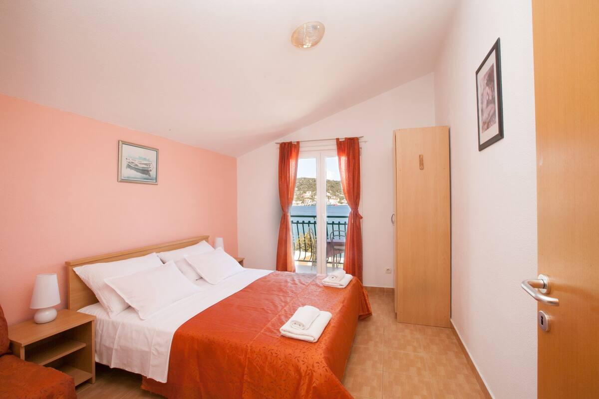 A bedroom with a bed, a nightstand, a door, and a window with curtains.