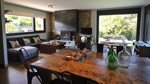 Uma sala de estar moderna com lareira, um espaço para refeições e amplas janelas com vista para o exterior.