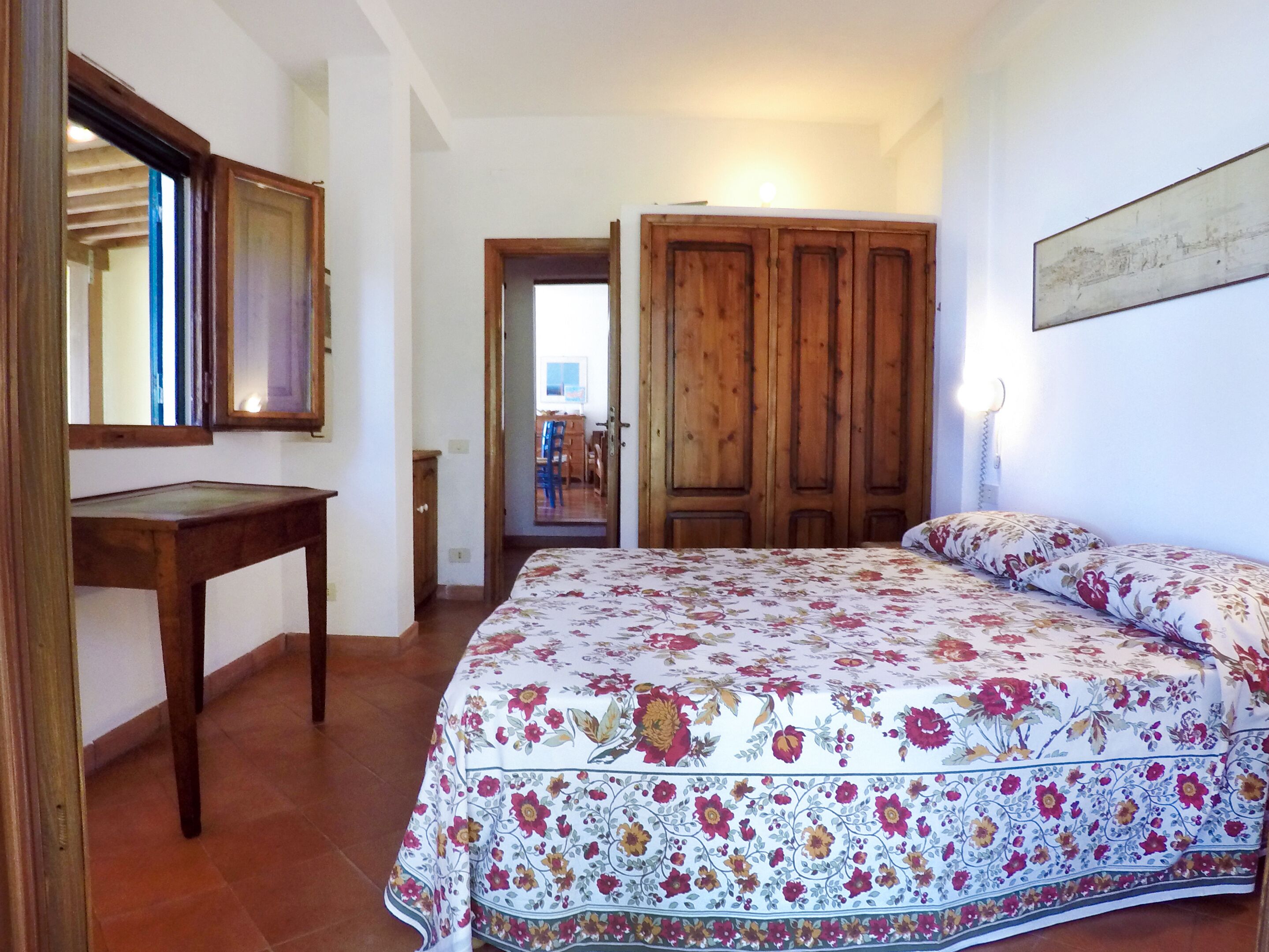 A bedroom with a bed, a wooden wardrobe, a desk, and a mirror.