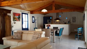 Uma sala de estar aconchegante com sofá, mesa de jantar com cadeiras, cozinha com micro-ondas e teto de madeira.