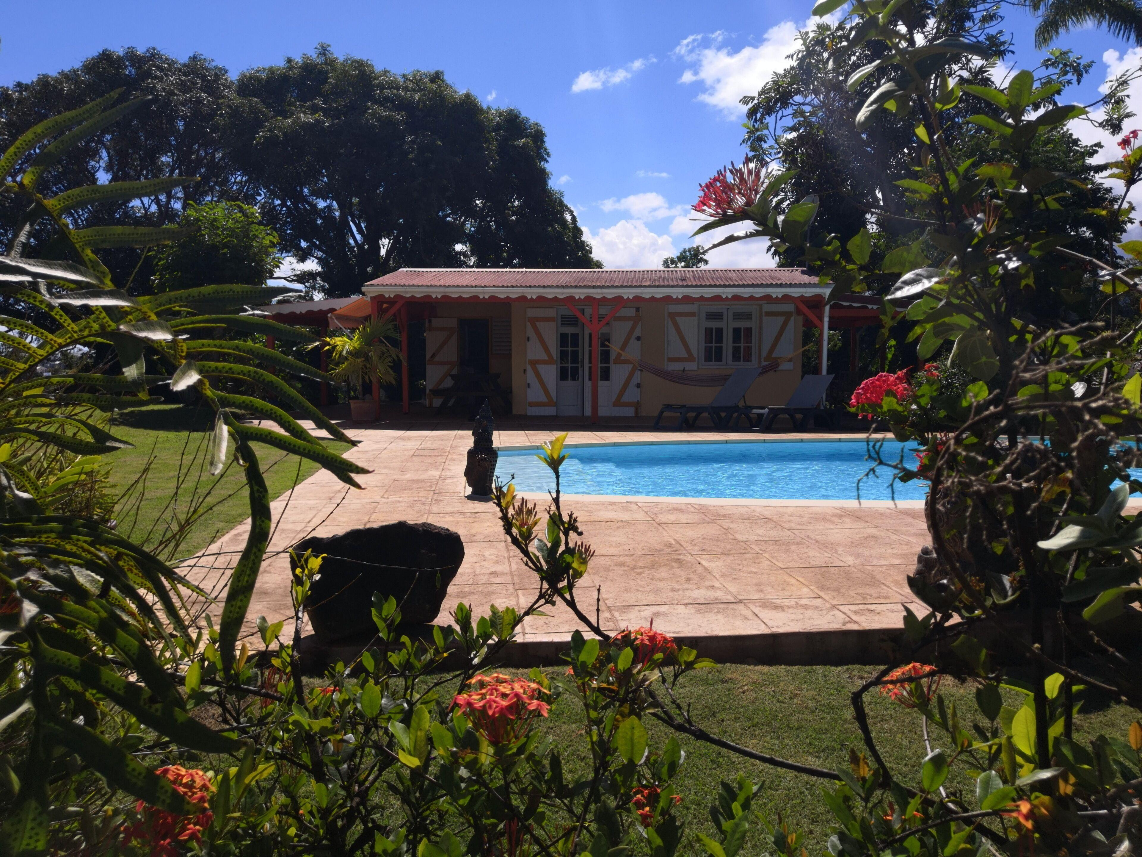 A pool area with a tiled deck, a hammock, and a building with a red roof in the background.