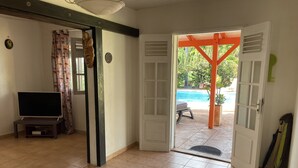 Une porte ouverte donnant sur un espace piscine, un téléviseur dans la pièce et une porte ornée d’une sculpture en bois décorative.