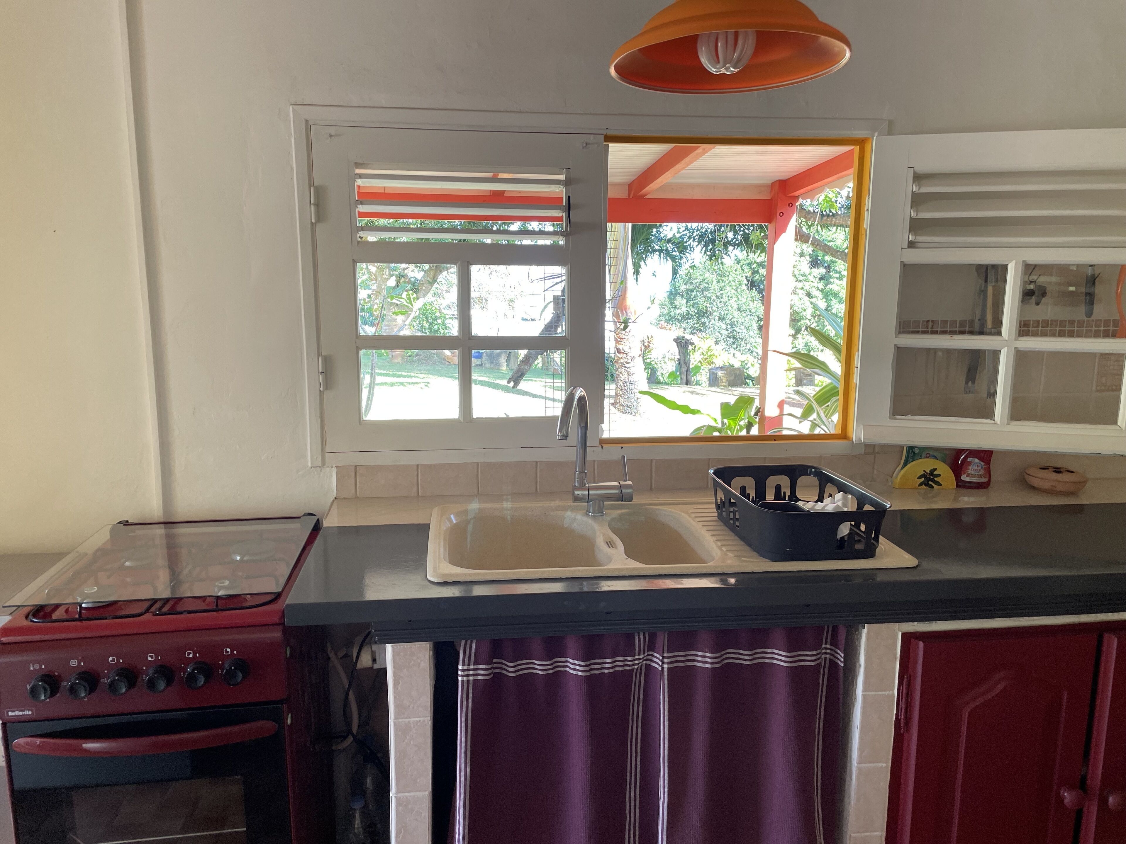 A kitchen with a red stove, a sink, and a window with a view of greenery.