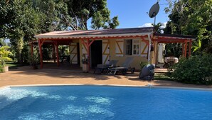 Un espace aménagé au bord de la piscine, comprenant un coin salon couvert, une piscine et une végétation luxuriante.