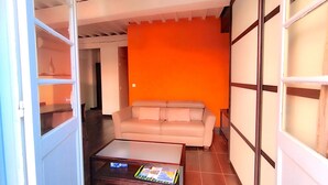 Een woonkamer met een beige bank, een glazen salontafel en een fel oranje accentmuur.