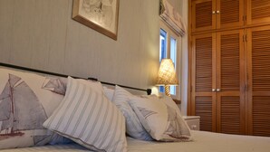 A neatly made bed with striped bedding and decorative pillows, a bedside lamp, and wooden wardrobe doors in the background.