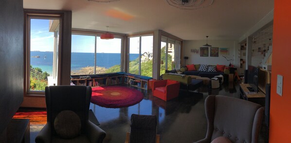A spacious living room with a large window offering a view of the sea and a balcony.