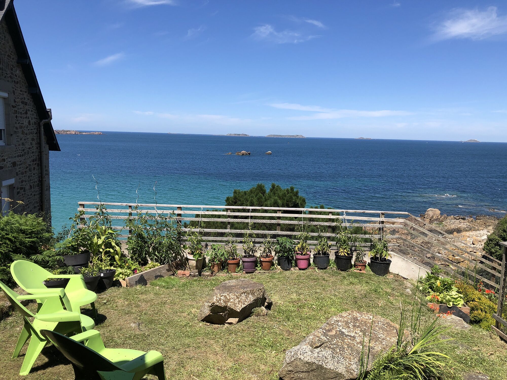 Une terrasse avec vue sur la mer, des plantes en pot et un fauteuil vert.