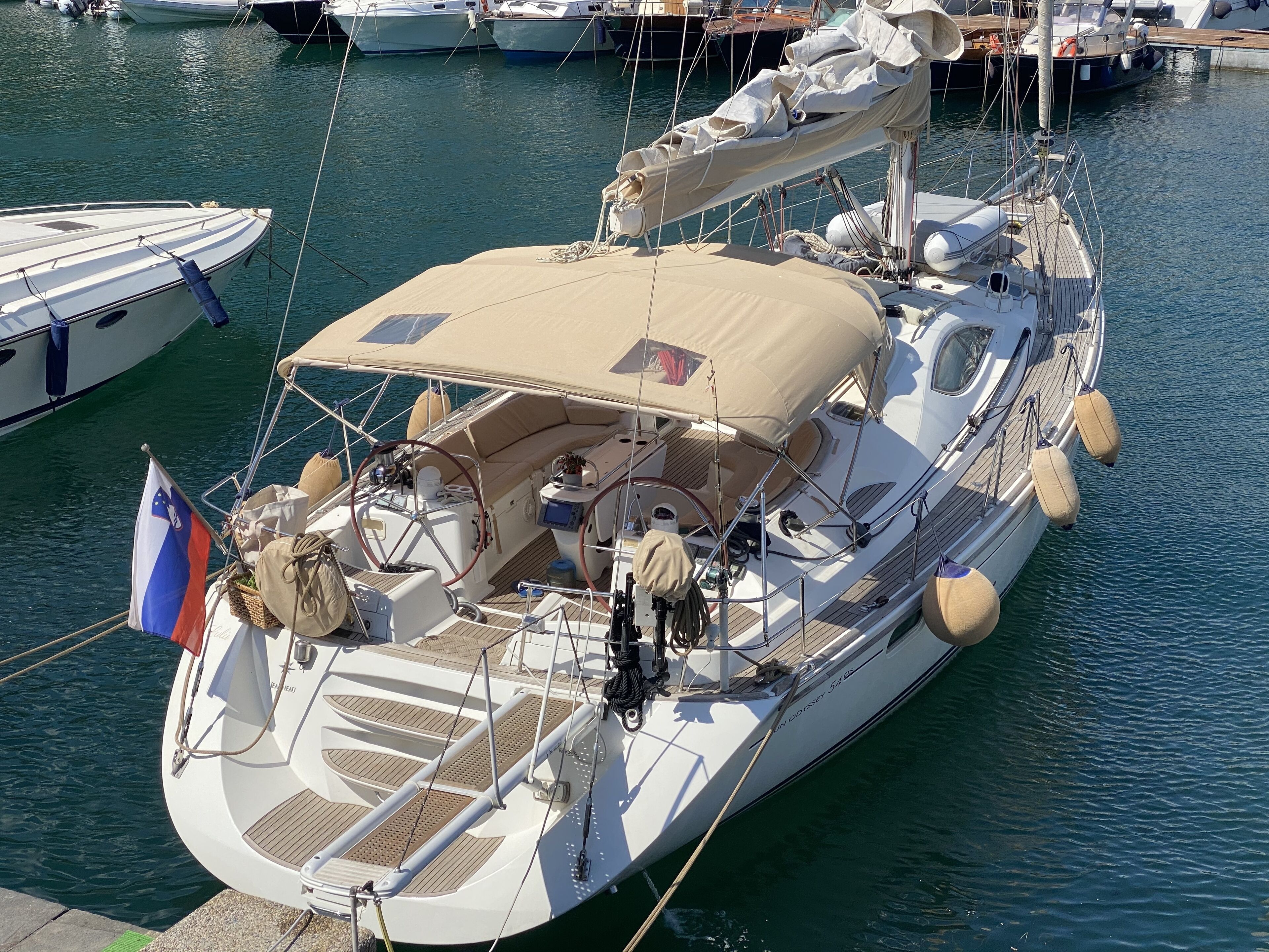 A yacht docked at a marina with a covered deck, multiple seating areas, and a flag.