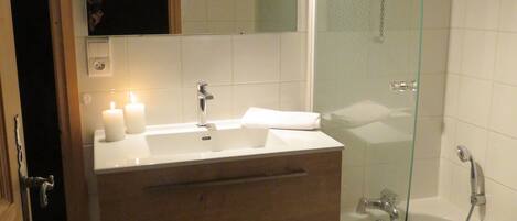 A modern bathroom with a glass-enclosed shower, a vanity with a mirror, and a wooden cabinet.