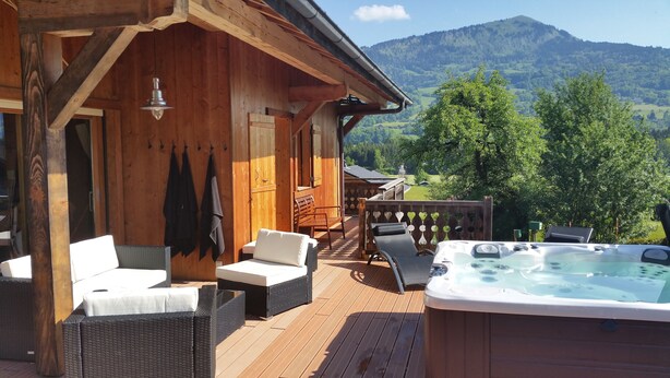 Eine Holzterrasse mit Korbmöbeln, einem Whirlpool und Blick auf grüne Hügel.