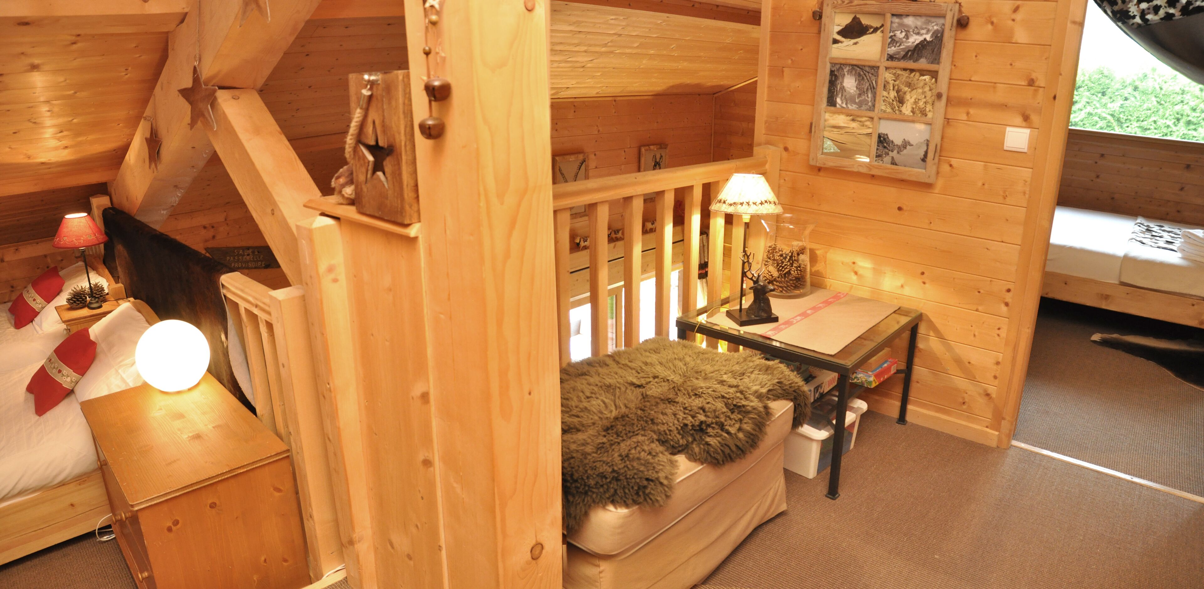 A cozy cabin room with a bed, a small table with a lamp, a window with a view, and a wooden wall with a star decoration.