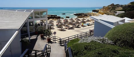 A beachside hotel with a wooden staircase leading to a deck with beach umbrellas and lounge chairs.