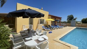A poolside area with sun loungers, a table set for dining, and a clear blue sky. - Beautiful Villa with Relaxing Atmosphere. 4 Bedrooms, 4 Bathrooms, Large & Fenced Pool 8-10 persons (Ferreiras)