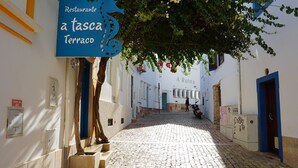 A cobblestone street with a restaurant sign, a tree, and a building with a blue door. - Beautiful Villa with Relaxing Atmosphere. 4 Bedrooms, 4 Bathrooms, Large & Fenced Pool 8-10 persons (Ferreiras)