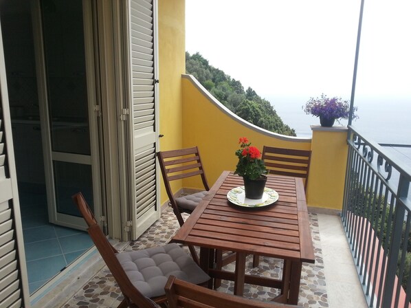 A balcony with a wooden table and chairs, a potted plant with red flowers, and a view of the sea. - HOUSE WITH PRIVATE PARKING AND MAGNIFICENT VIEW ON THE BAY OF POSITANO (Positano)