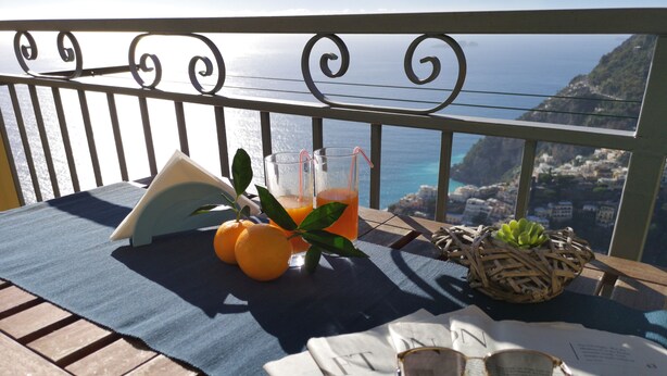 Ein Tisch mit einem Buch, einer Brille und einem Getränk auf einem Balkon mit Meerblick.
