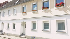 Un bâtiment à deux étages avec des murs blancs, de nombreuses fenêtres dotées de volets et un toit recouvert de tuiles.