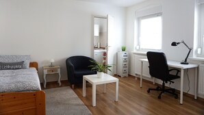 Une chambre à coucher comprenant un lit, un bureau, une chaise, une petite table, une plante en pot et une commode.