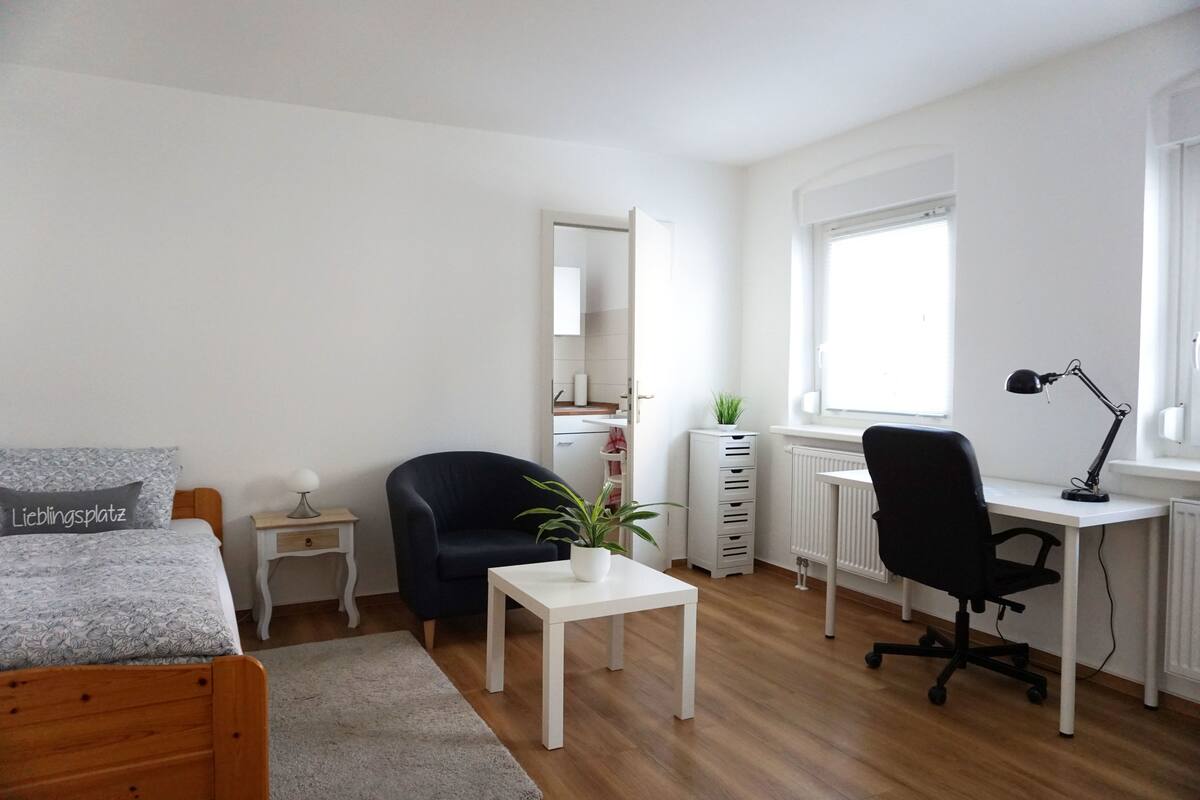 Une chambre à coucher comprenant un lit, un bureau, une chaise, une petite table, une plante en pot et une commode.