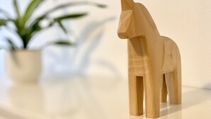 Une figurine de cheval en bois sur une surface blanche, avec une plante floue en arrière-plan.