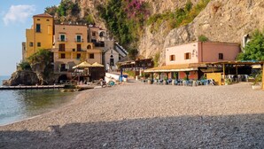 A coastal building with multiple balconies, a terrace with outdoor seating, and a rocky cliff backdrop. - Casa della Marina · Historic beachfront tonnara with direct sea access (Conca dei Marini)