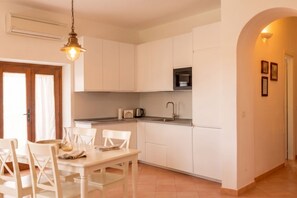 A modern kitchen with white cabinets, a black microwave, and a dining area with a white table and chairs.