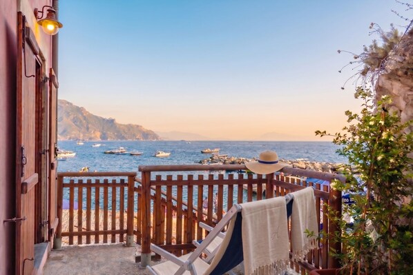 A balcony with a view of the sea and boats, a wooden railing, and a chair with a towel.